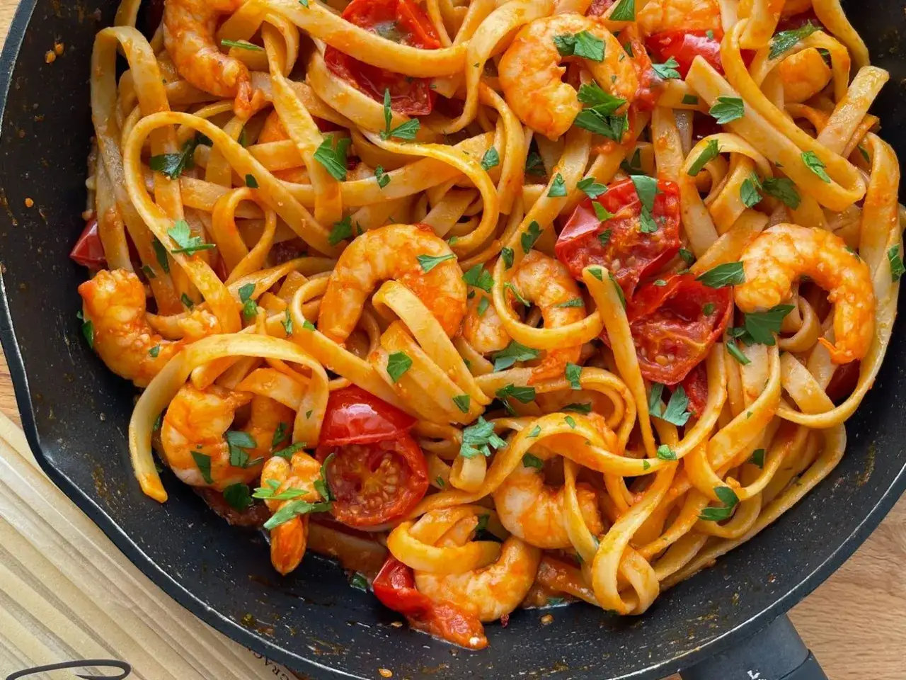 Pasta con mazzancolle succulenta, condita con pomodorini e prezzemolo fresco, servita in una padella scura.