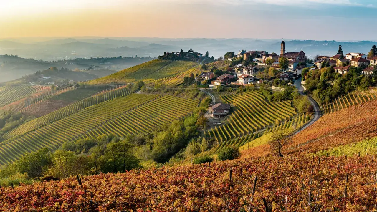 Dolci colline del Piemonte in autunno, con vigneti colorati e un borgo. Ideale per esplorare i **percorsi enogastronomici Piemonte**.