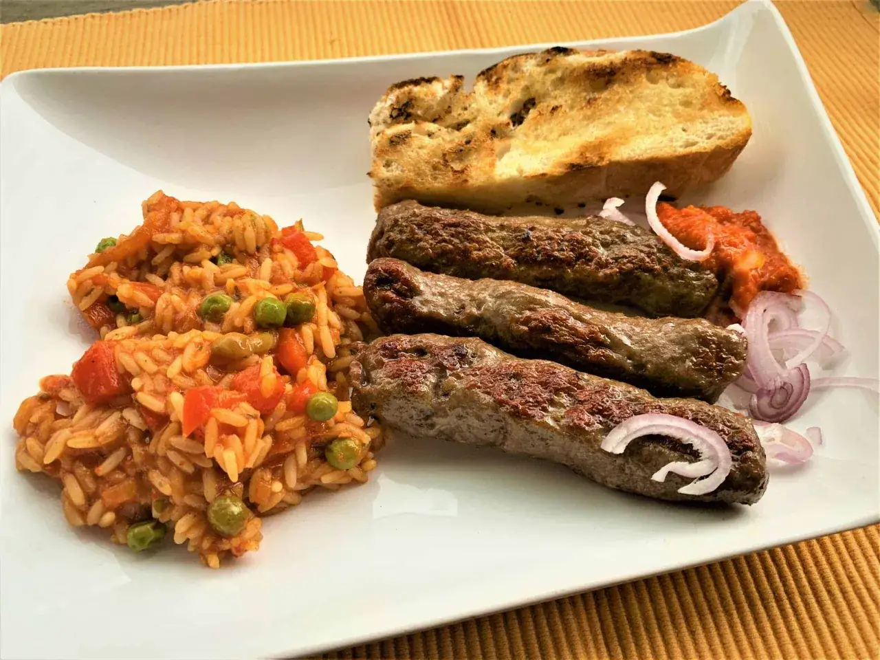 Drei Cevapcici, Reis mit Gem&uuml;se, gegrilltes Brot und Zwiebelringe &ndash; so einfach kann man Cevapcici selber machen und genie&szlig;en.