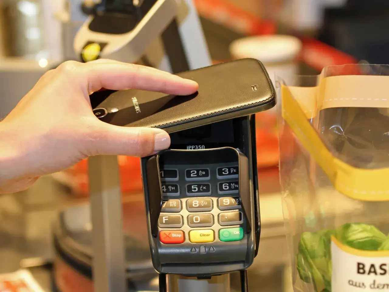 Nahaufnahme einer Hand, die ein Smartphone &uuml;ber ein Kassenterminal h&auml;lt. Gute openbank erfahrungen mit kontaktlosem Bezahlen.