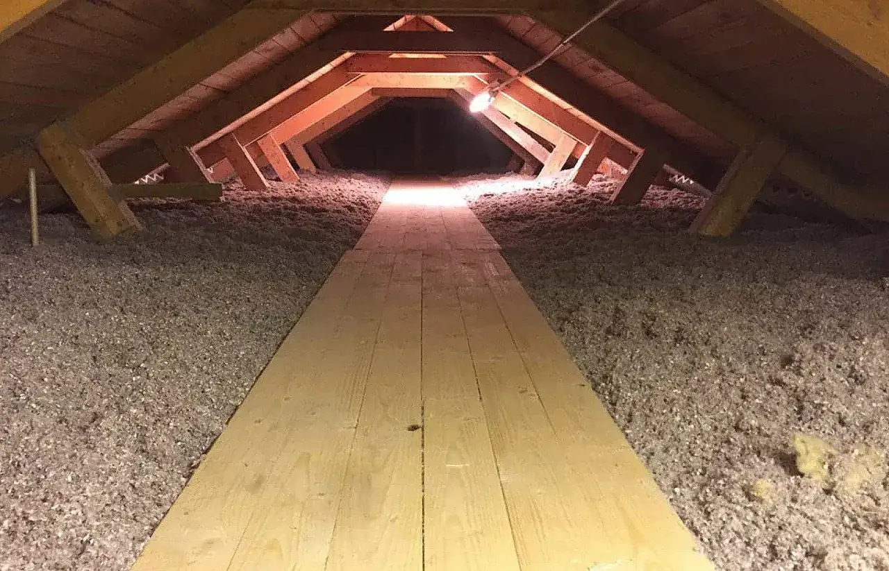 En gångväg av träplankor leder genom ett isolerat vindsutrymme med fluffig isolering på sidorna.