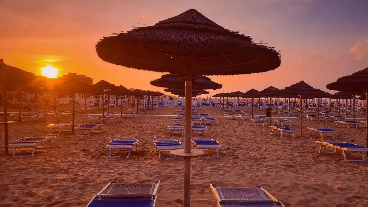 Zachód słońca nad pustą plażą w Rimini. Rzędy leżaków i parasoli tworzą spokojny krajobraz.