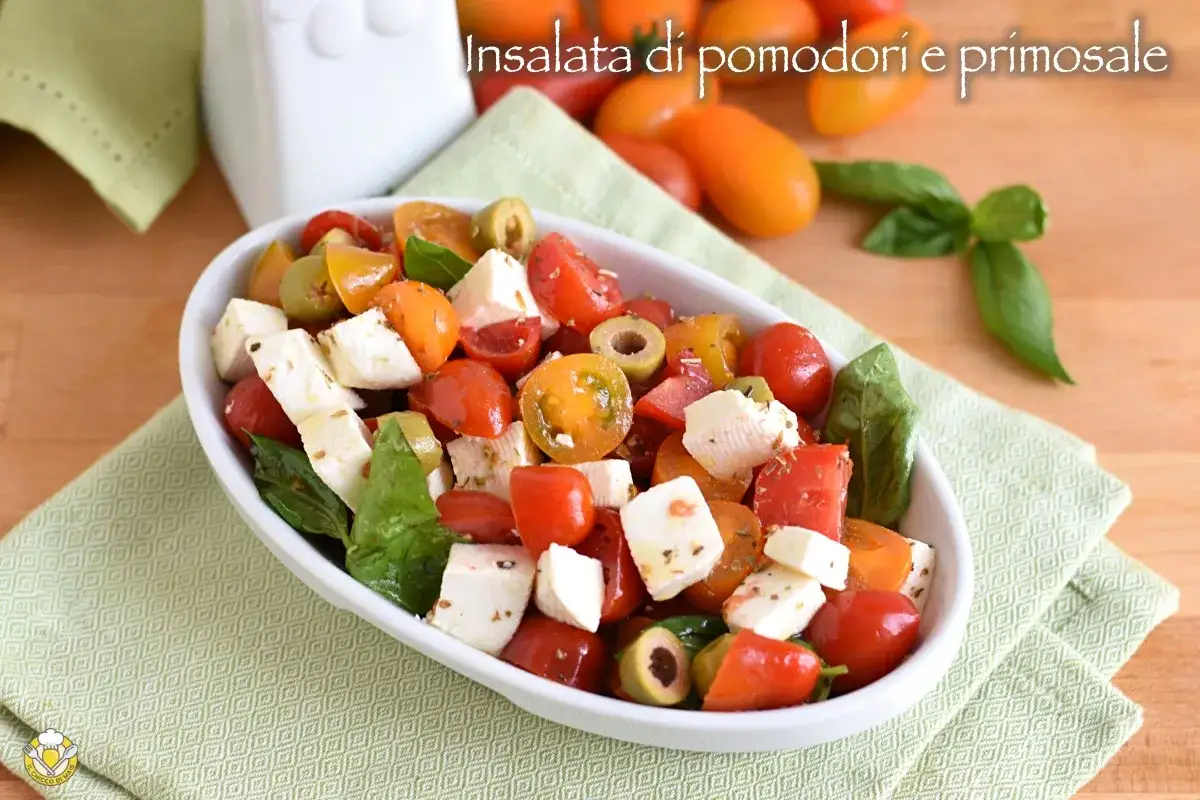 Insalata estiva con pomodorini colorati, cubetti di primo sale fresco e olive verdi, condita con basilico.