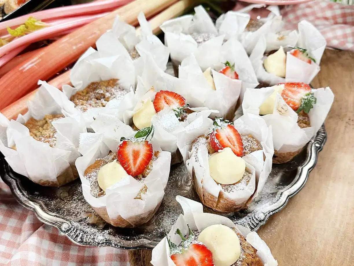 En bricka med rabarber muffins, toppade med vaniljkräm och färska jordgubbar.