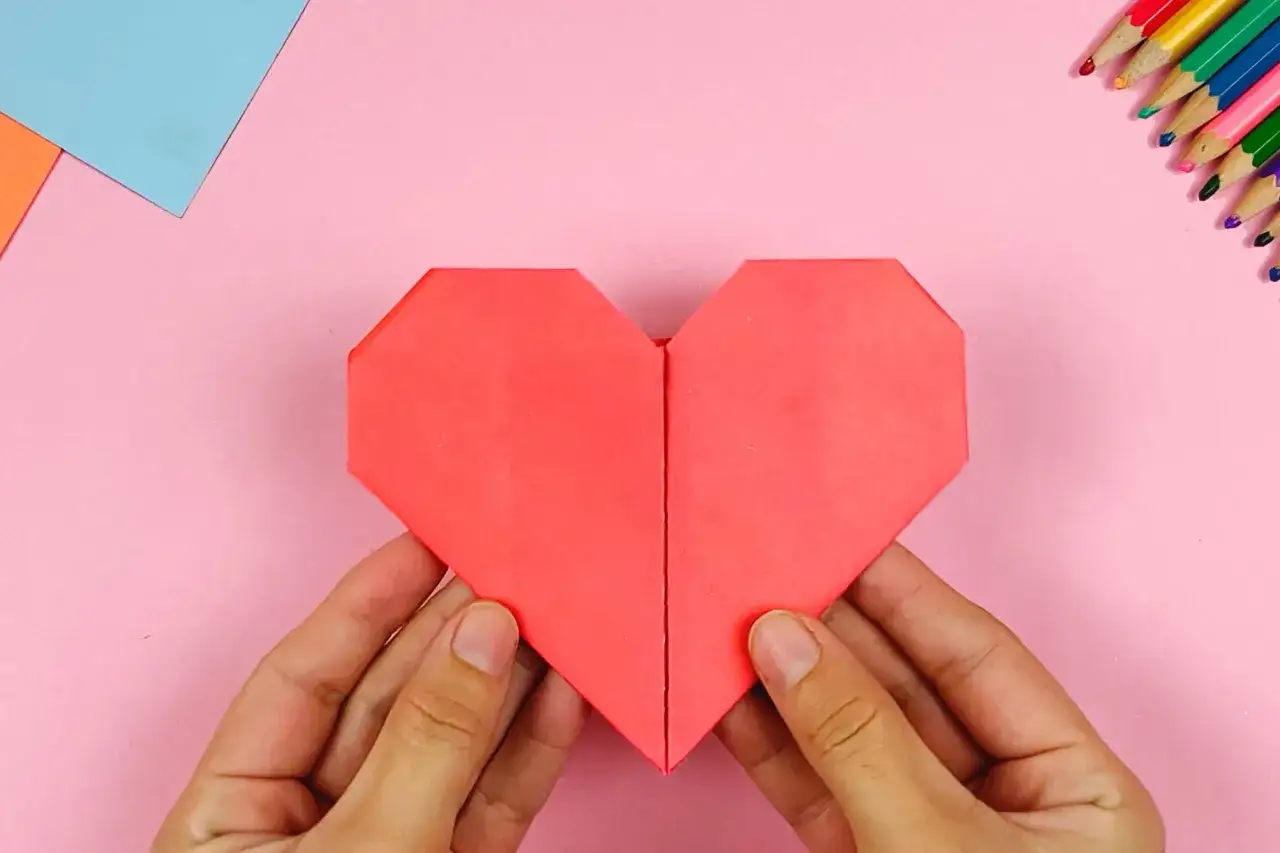 H&auml;nde falten ein rotes Papierherz. Perfekt zum **Herzen basteln** f&uuml;r Valentinstag oder als Dekoration.