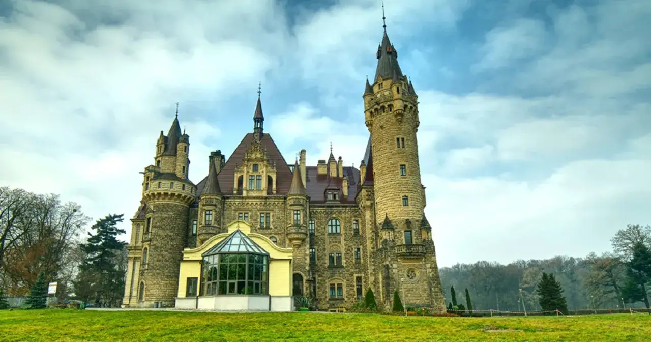 Zamek Moszna, jedna z najpiękniejszych opolskie atrakcje, z imponującymi wieżami i bogatą architekturą, na tle błękitnego nieba z chmurami.