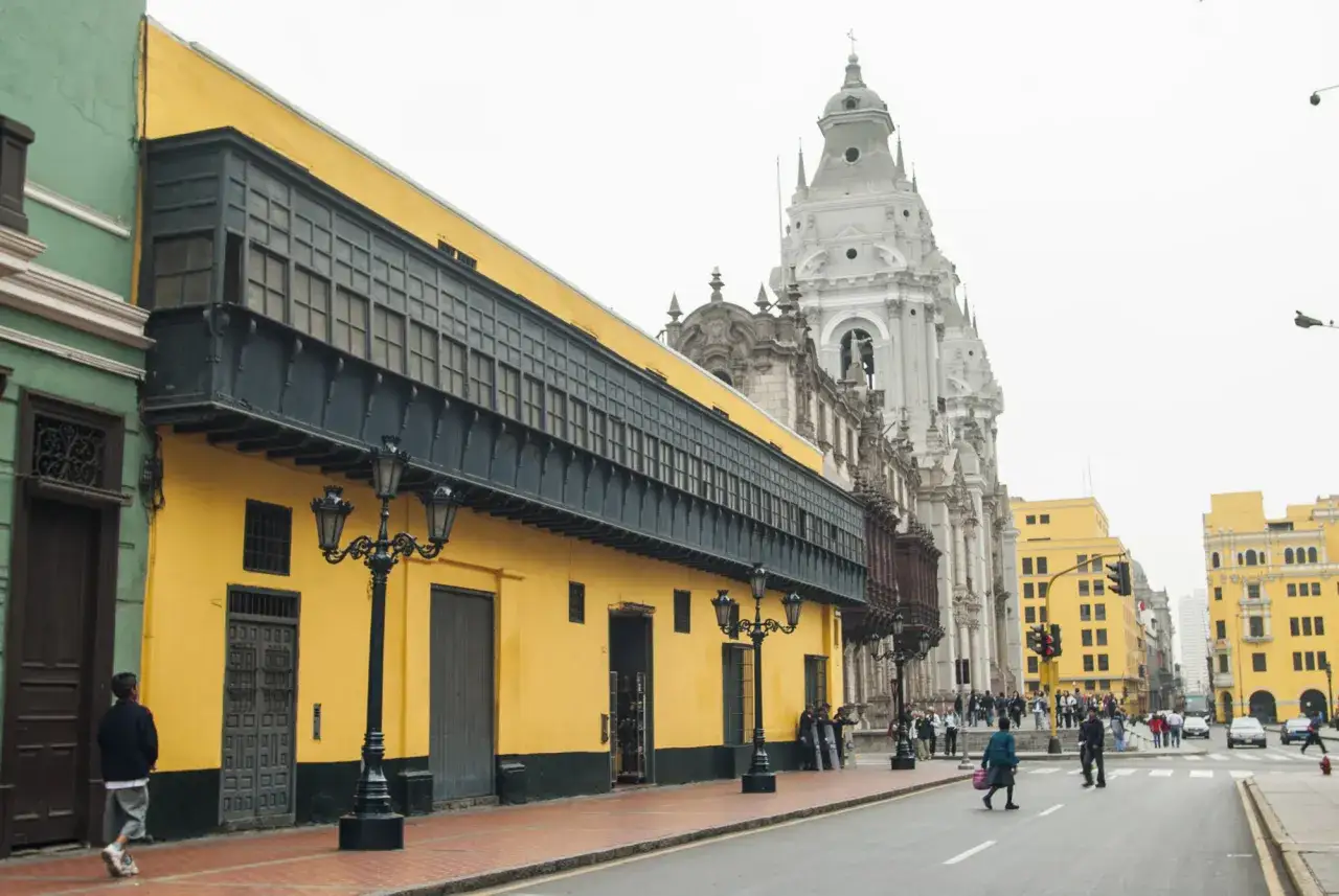 Edificios coloniales amarillos y verdes con balcones de madera, una iglesia blanca y gente paseando. Ideas de qué hacer en Lima.