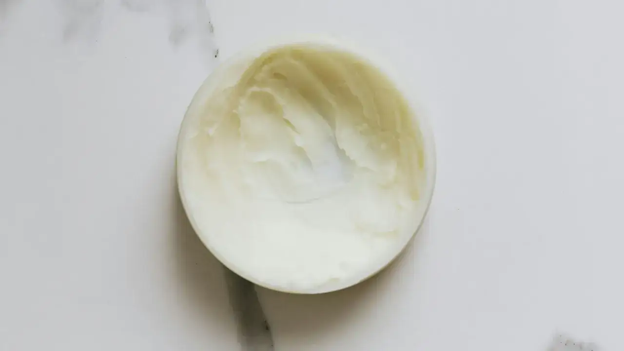 Biały krem z cetearyl alcohol w okrągłym pojemniku, na marmurowym tle.