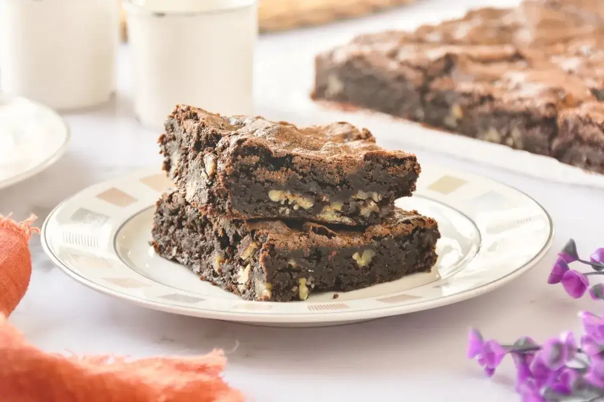 Dos deliciosos trozos de brownie sin gluten apilados en un plato, con nueces visibles.