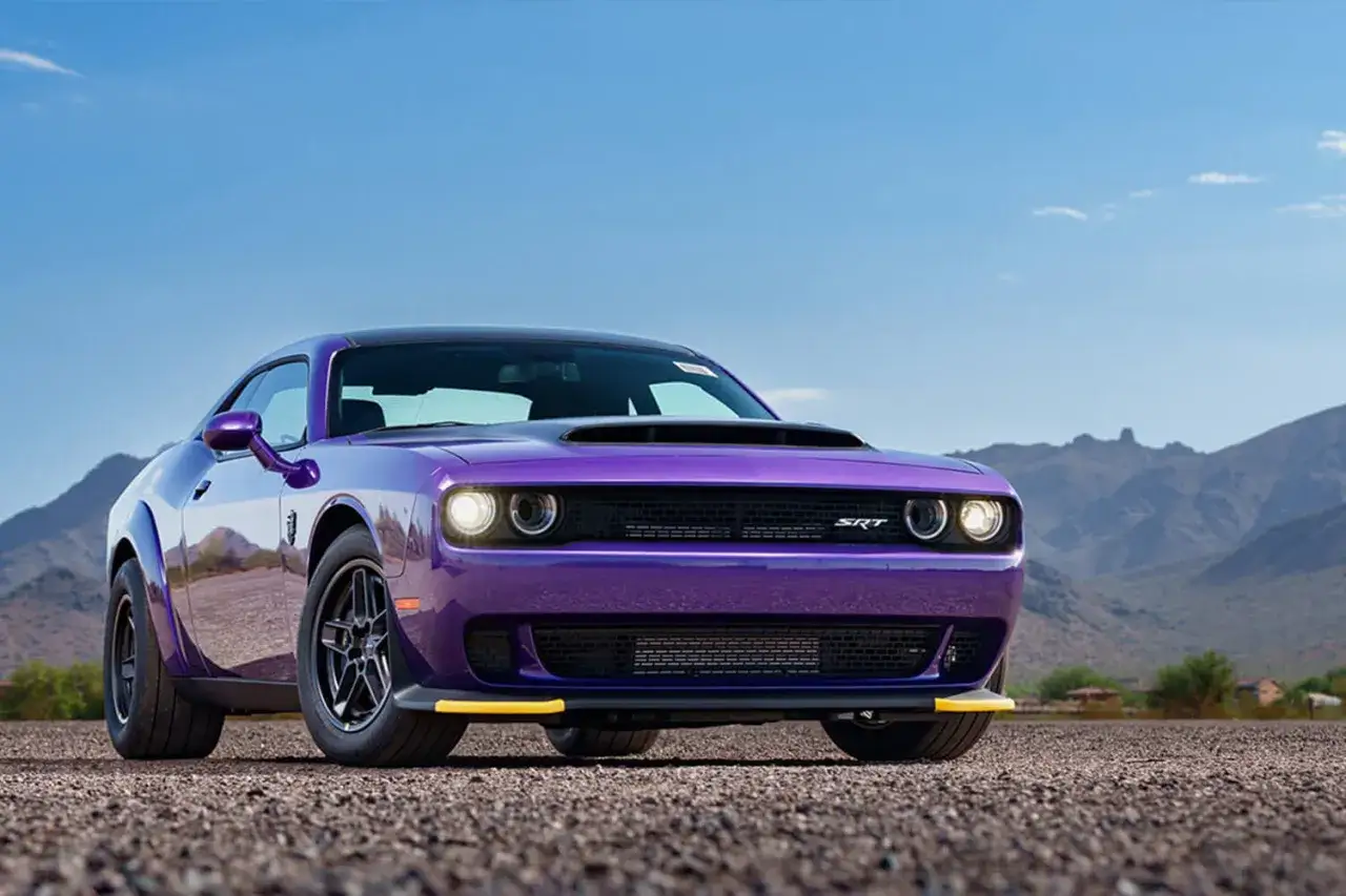 Lila Dodge Demon 170 mit gelben Akzenten steht auf Schotter vor einer Bergkulisse.