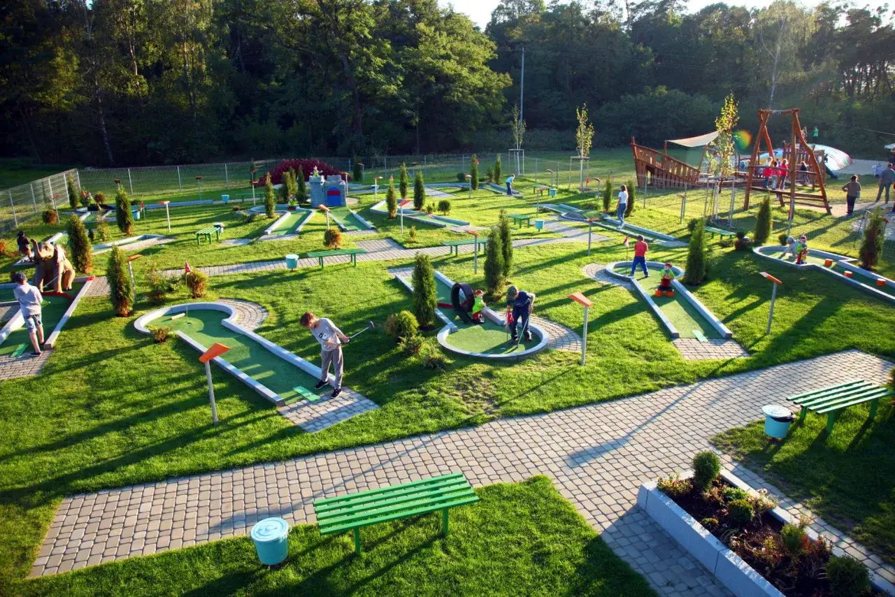 Park rozrywki Julinek tętni życiem. Dzieci grają w minigolfa wśr&oacute;d zieleni i słońca.
