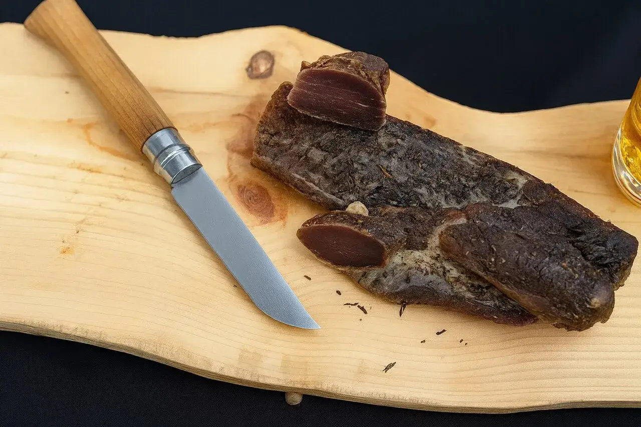 Un couteau et un morceau de filet mignon séché sur une planche en bois. Une tranche est coupée, révélant la chair rouge.