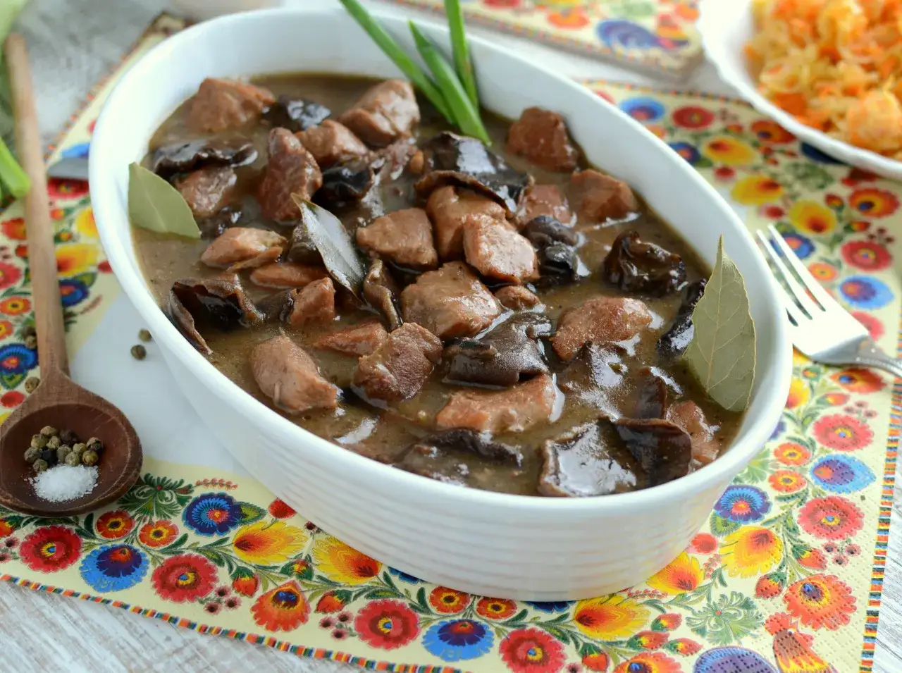 Gulasz z grzybami suszonymi, mięsem i liśćmi laurowymi w białej misie, na kolorowym obrusie.