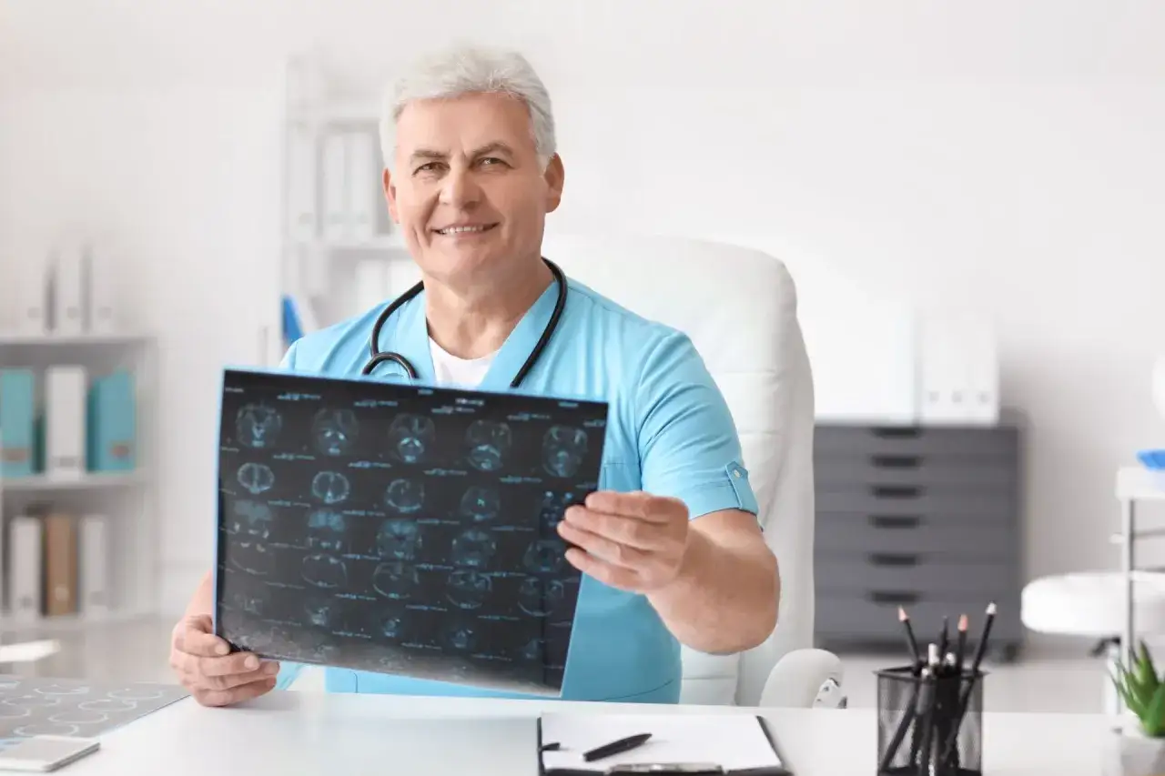 Uśmiechnięty lekarz pokazuje wyniki rezonansu mózgu. Czy do neurologa potrzebne jest skierowanie? Zapytaj swojego lekarza rodzinnego.