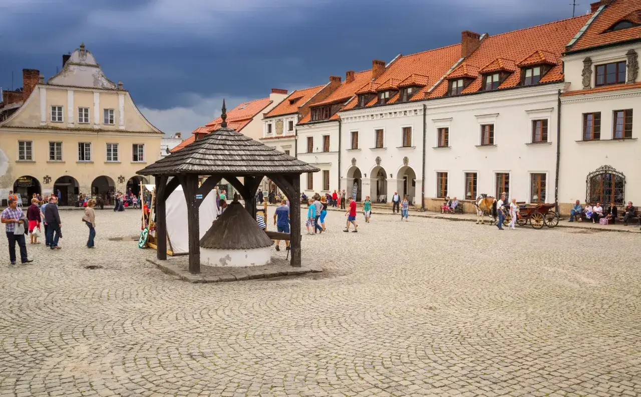 Rynek w Kazimierzu Dolnym z brukowaną nawierzchnią, drewnianą studnią i zabytkowymi kamienicami.