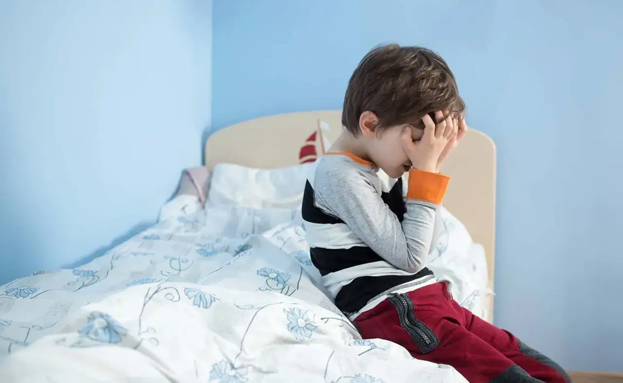 Niño triste en la cama, preocupado por la enuresis nocturna infantil. Busca remedios naturales para superarla.