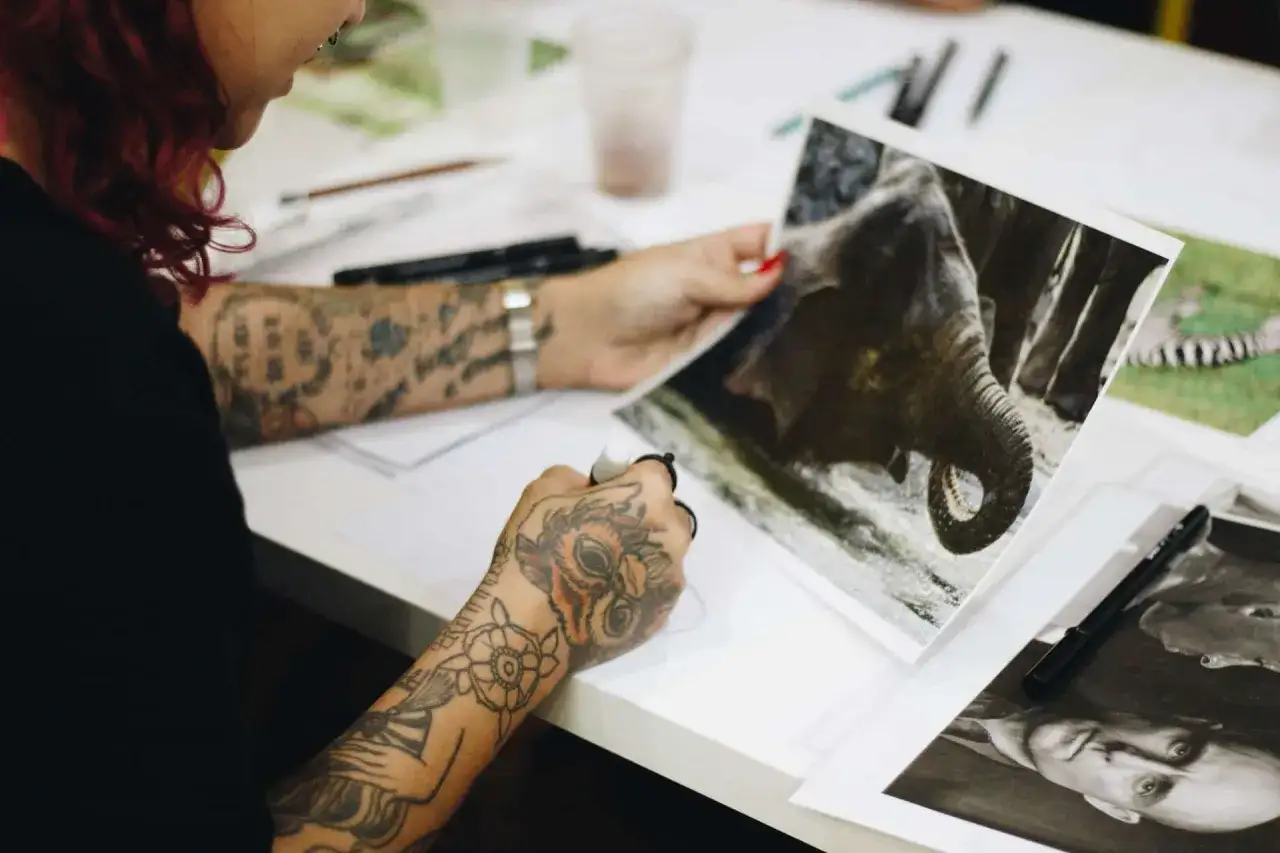 Une personne tatouée étudie des photos d'éléphants et de portraits, préparant sa prochaine création lors d'une formation dessin tatouage.
