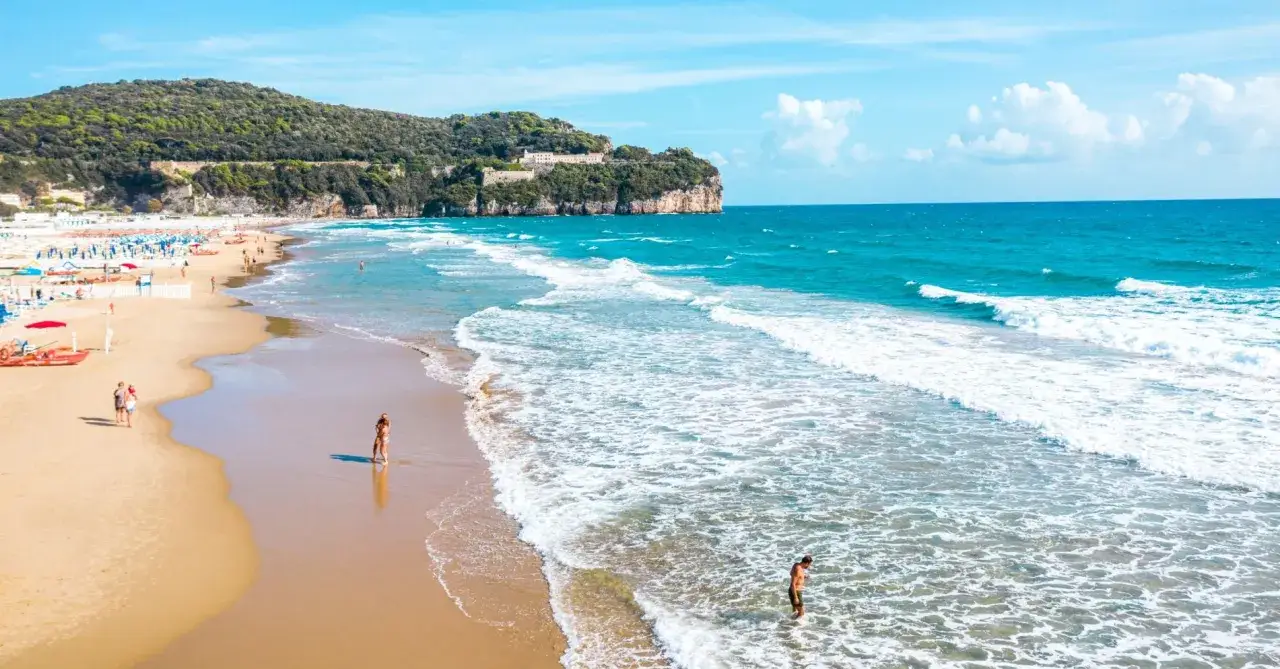 Spiaggia dorata con onde turchesi, una località di mare tra Lazio e Toscana, con persone che si godono il sole e il mare.