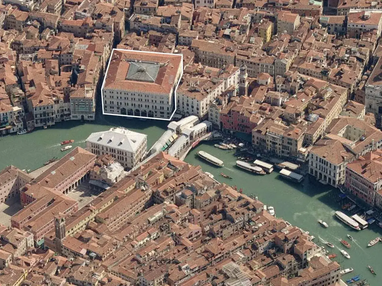 Venezia: un palazzo storico, forse un fondaco dei Tedeschi, si affaccia sul Canal Grande, circondato da tetti rossi e acque verdi.