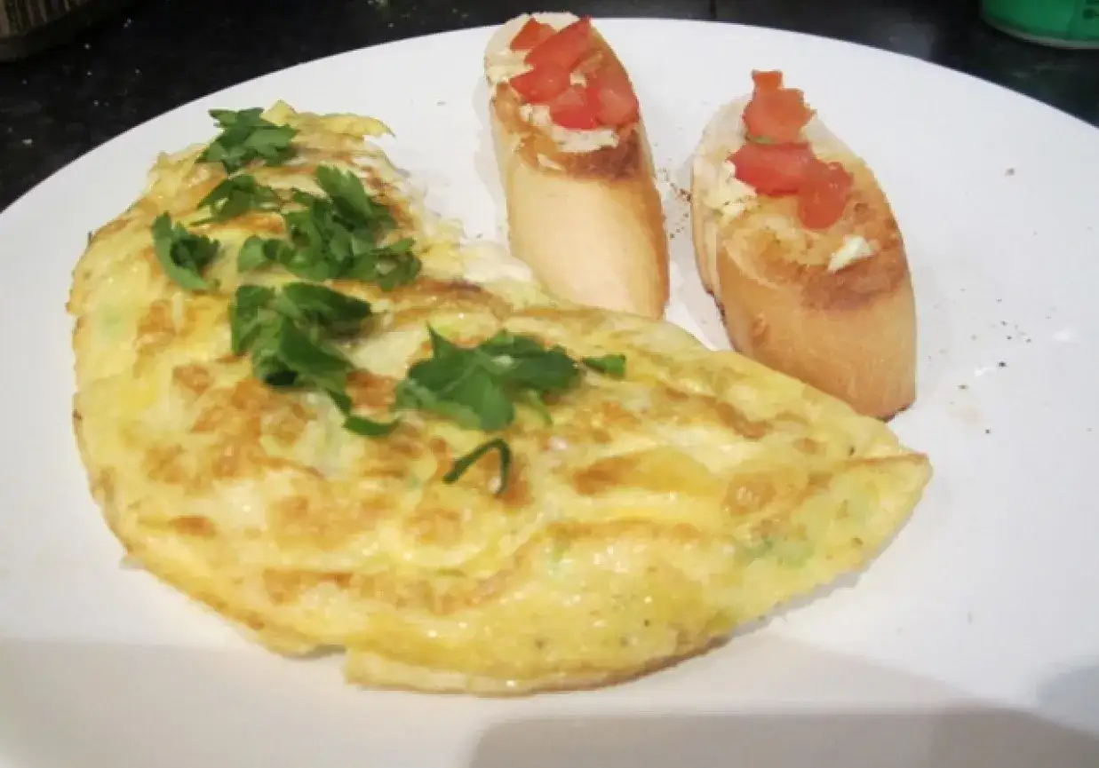 Pyszny omlet na słono, udekorowany świeżą natką pietruszki, podany z chrupiącymi grzankami z pomidorami.