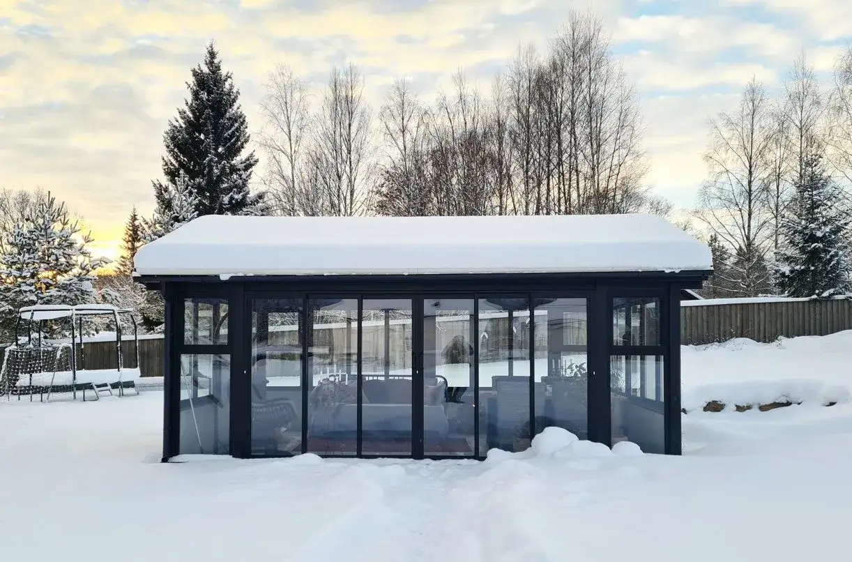 Ett modernt uterum med glasväggar och snö på taket. En dröm att bygga uterum för att njuta av vintern.