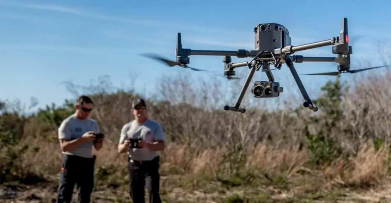 Dwóch mężczyzn ćwiczy kurs latania dronem. W powietrzu unosi się profesjonalny dron z kamerą.