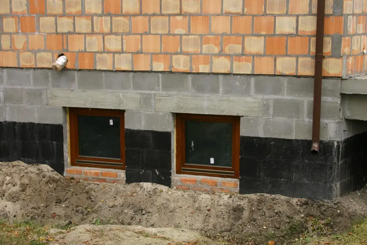 Fundamenty starego domu z oknami piwnicznymi i izolacją przeciwwilgociową. Rozważasz, czy ocieplać fundamenty w starym domu?