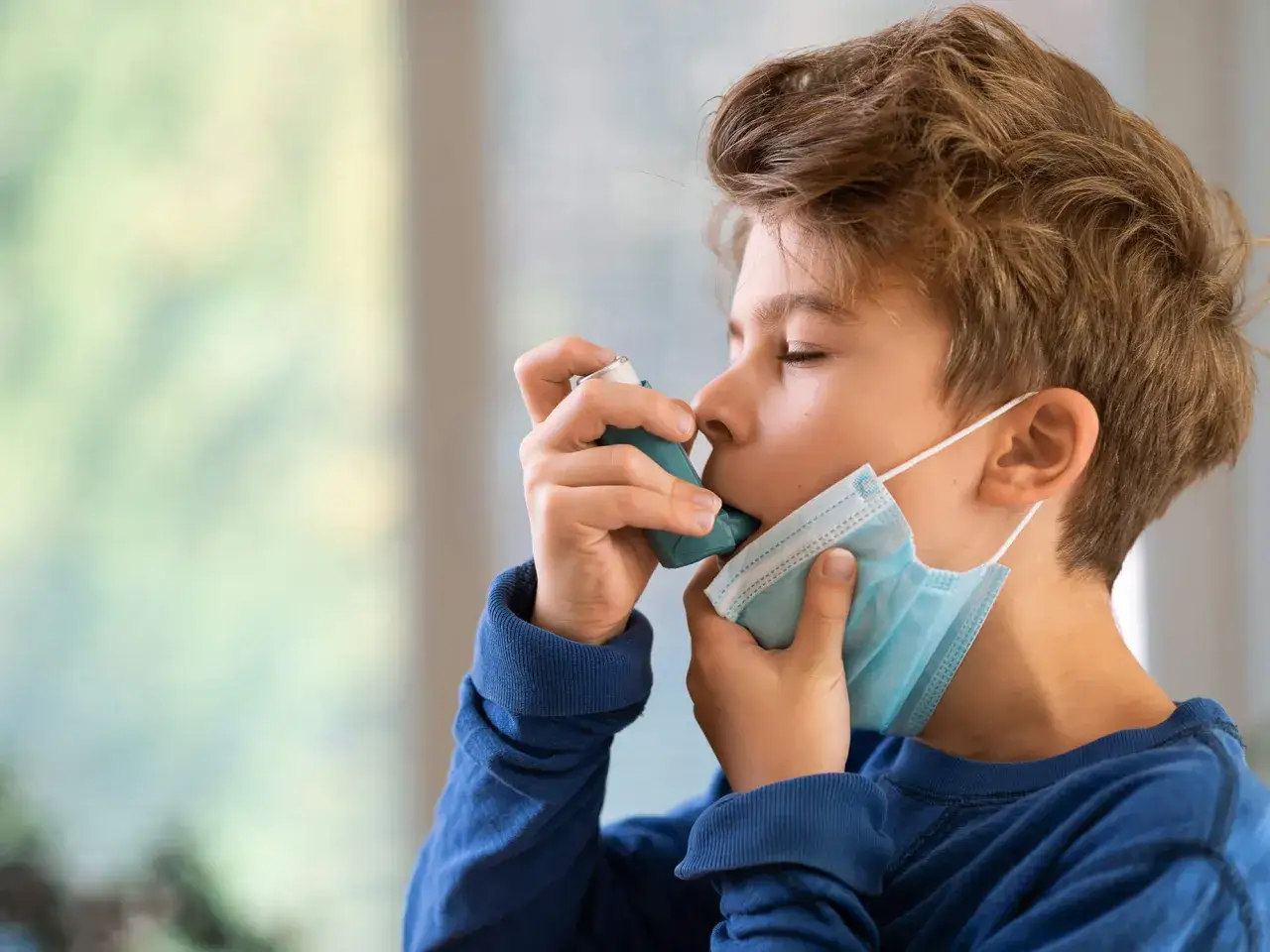 Junge mit Inhalator und Maske, der auf seine **Asthma**-Symptome achtet, besonders bei wechselnder **Luftfeuchtigkeit**.