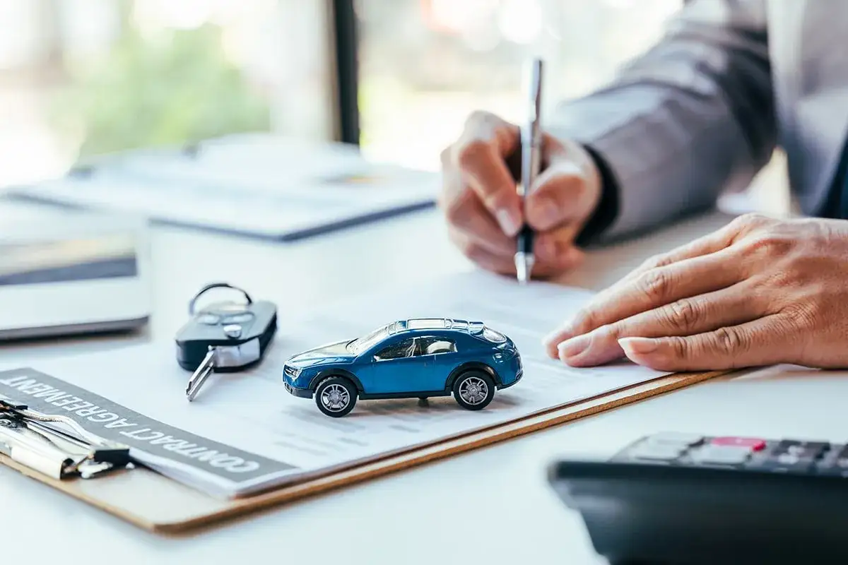 Signature d'un contrat d'assurance achat voiture, avec une cl&eacute; et une miniature de voiture sur le document.