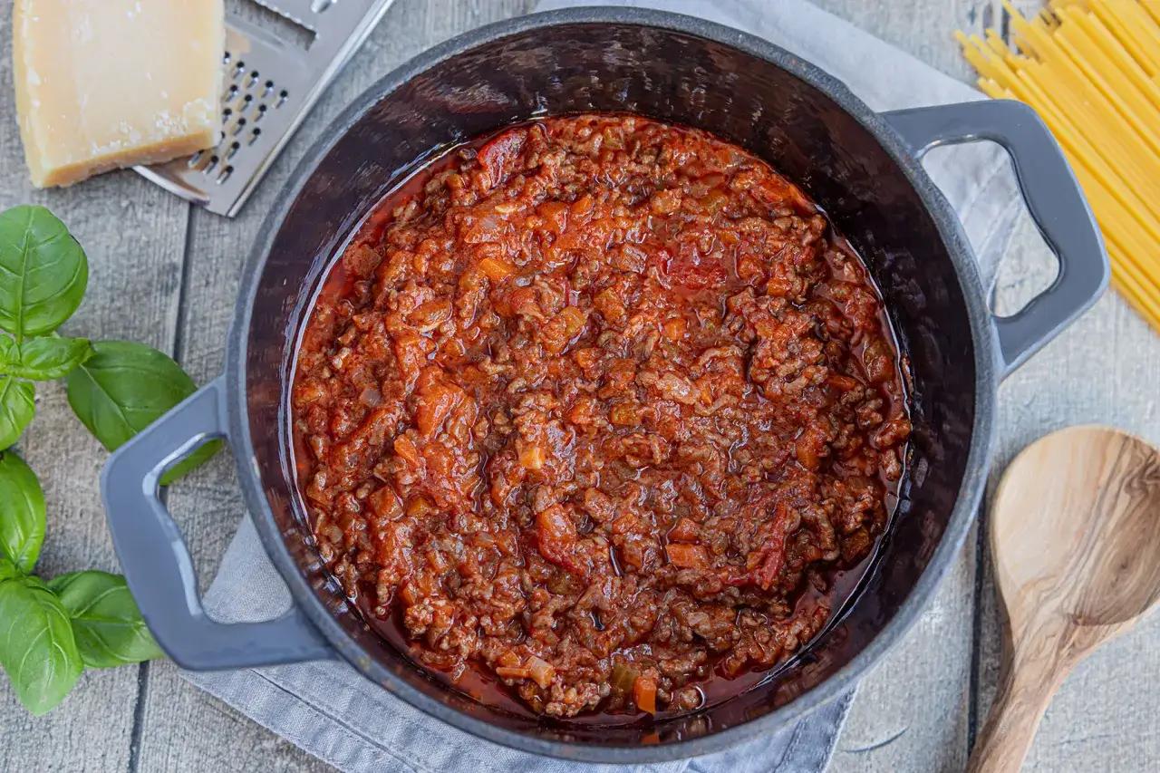 Herzhaftes Bolognese-Rezept in einem Topf, bereit für Spaghetti. Frisches Basilikum und Parmesan daneben.