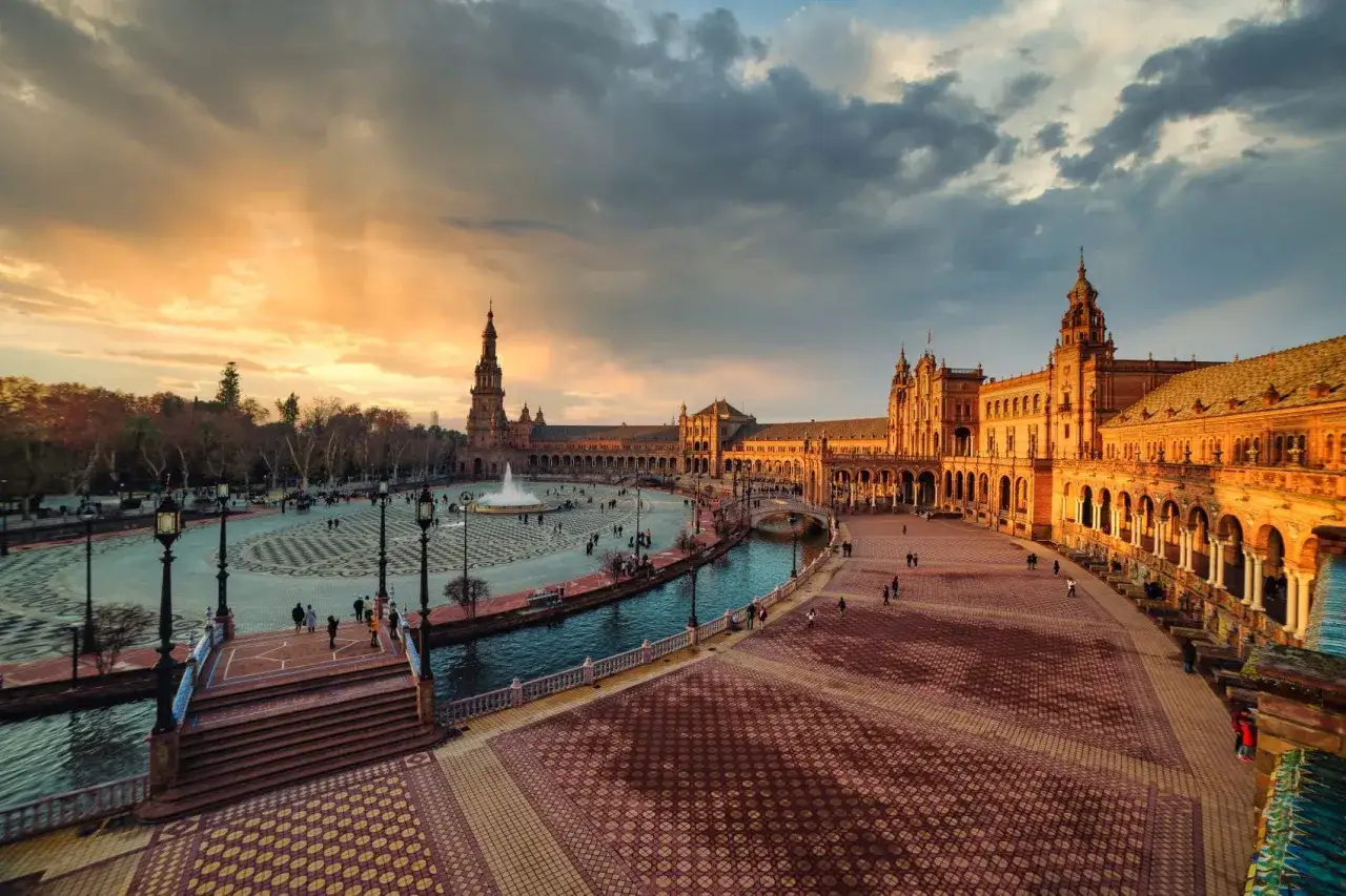 Plaza de España in Sevilla bei Sonnenuntergang. Ein Kanal schlängelt sich durch die Anlage, mit Menschen, die spazieren gehen. Wie viele Tage braucht man, um all das zu erkunden?