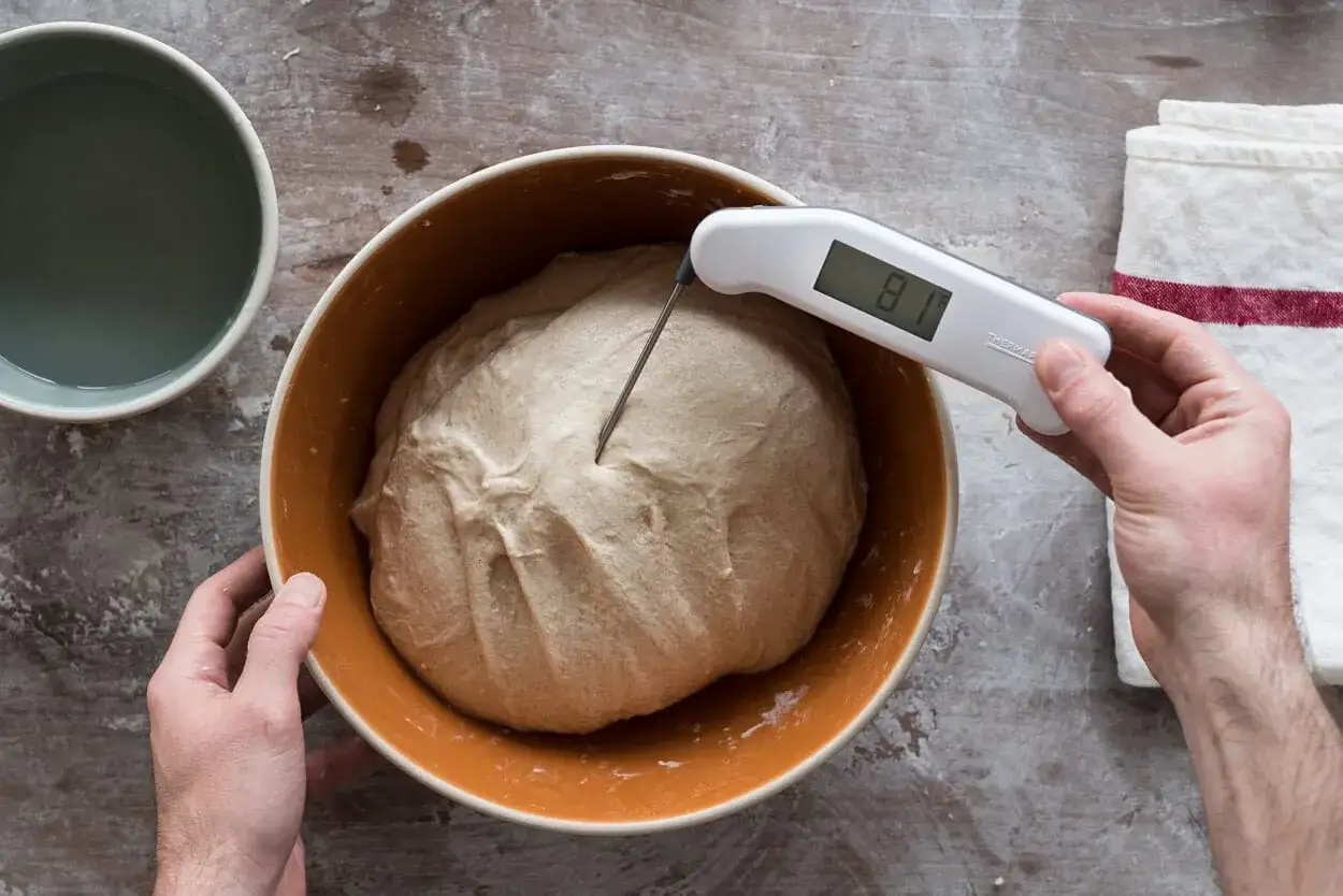 Pizzateig-Temperatur wird mit einem digitalen Thermometer gemessen. Der Teig ruht in einer orangen Schüssel.