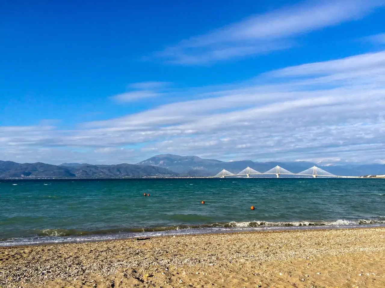 Piękna pogoda w Grecji w grudniu. Spokojne morze, piaszczysta plaża i most na horyzoncie.