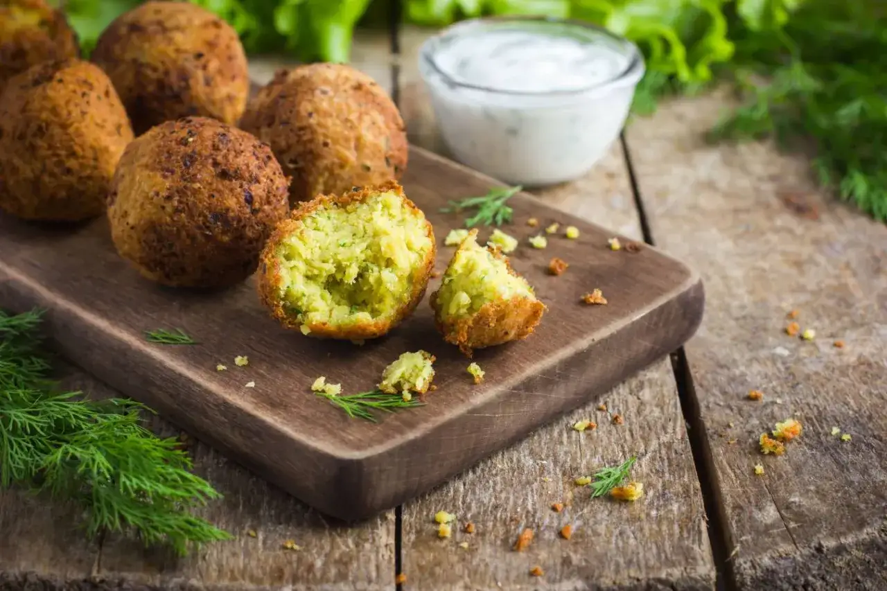 Falafel kebab co to? Chrupiące kulki falafela na desce, jedna przekrojona, z sosem i ziołami.
