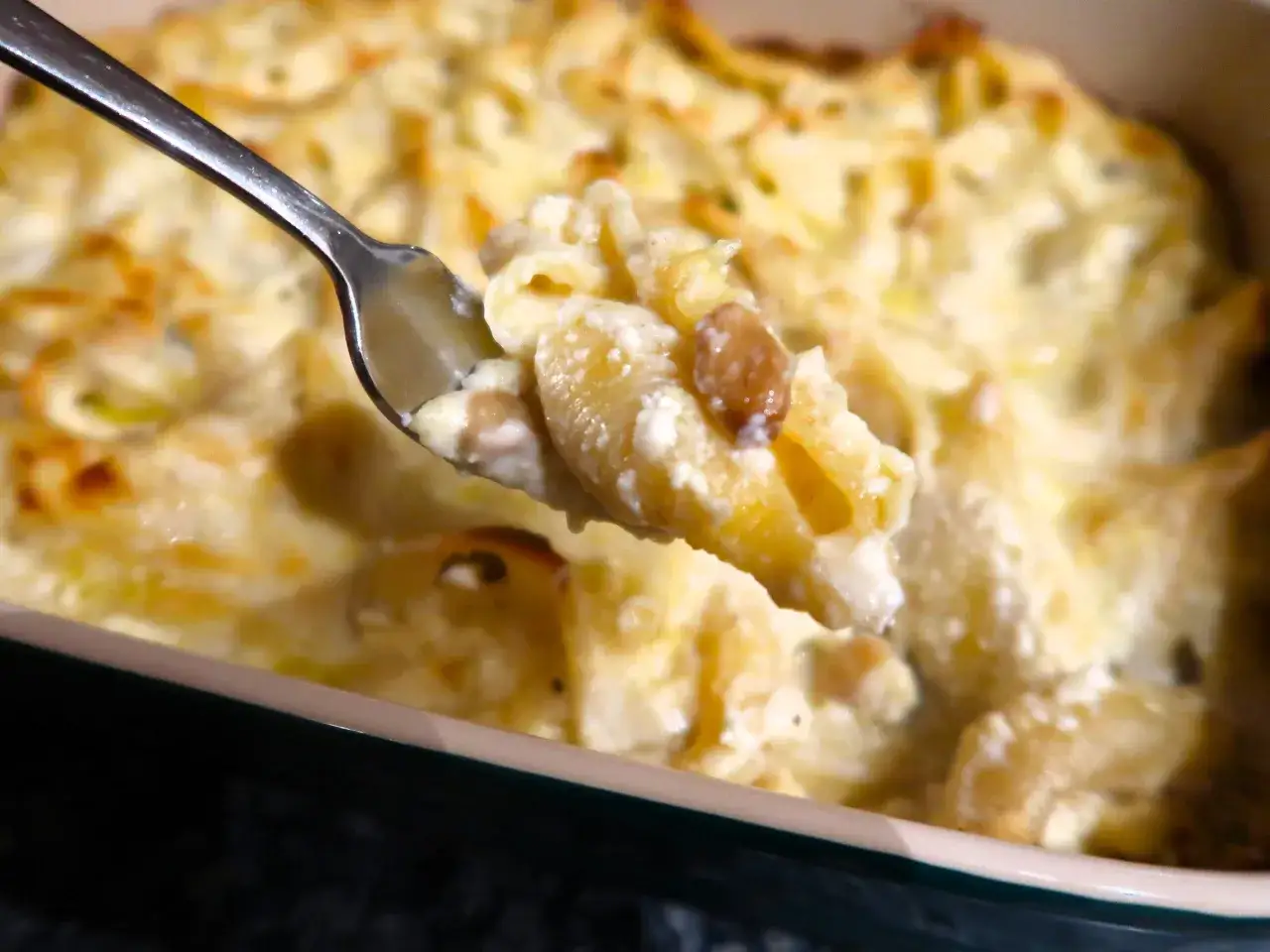 Une cuill&egrave;re de conchiglioni farcis aux champignons, cr&eacute;meux et dor&eacute;s, sort d'un plat gratin&eacute;.