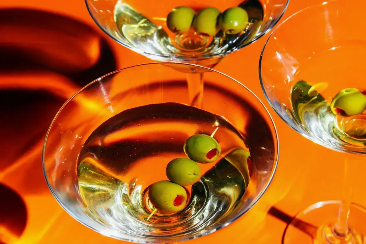 Trzy kieliszki z martini, każdy ozdobiony oliwkami. Idealne na wieczór, gdy zastanawiasz się, jak zrobić martini.