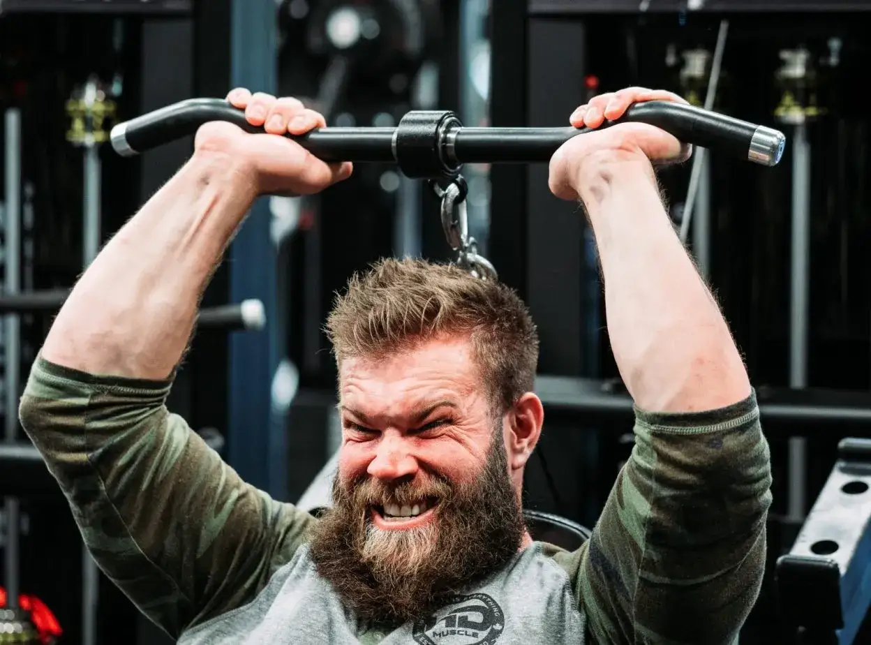 Hombre con barba haciendo extensión de triceps en máquina, concentrado y con esfuerzo.