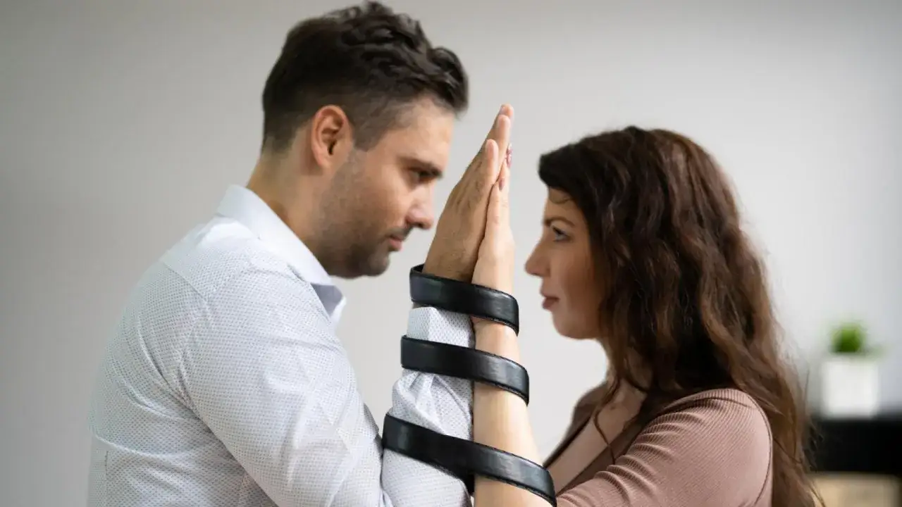 Pareja con las manos entrelazadas y atadas con una correa, simbolizando que la codependencia es una enfermedad que atrapa.