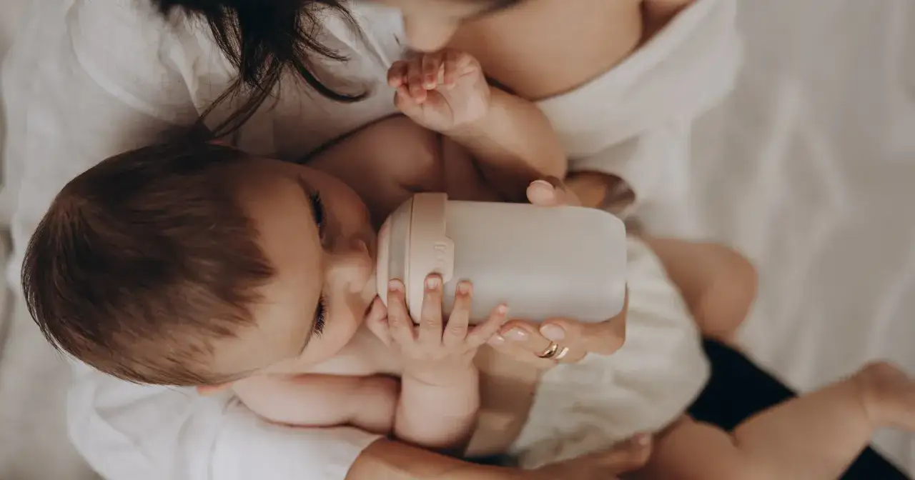 Mama karmi dziecko butelką. Czy można przekarmić noworodka? Delikatne dłonie malucha obejmują butelkę.