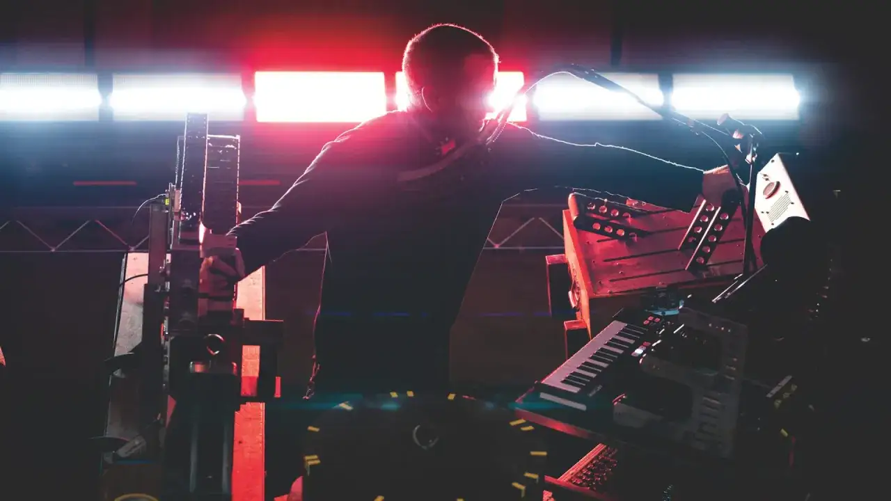 L'auteur, tel un punisher sonore, manipule des machines complexes sous des lumières rouges vives.