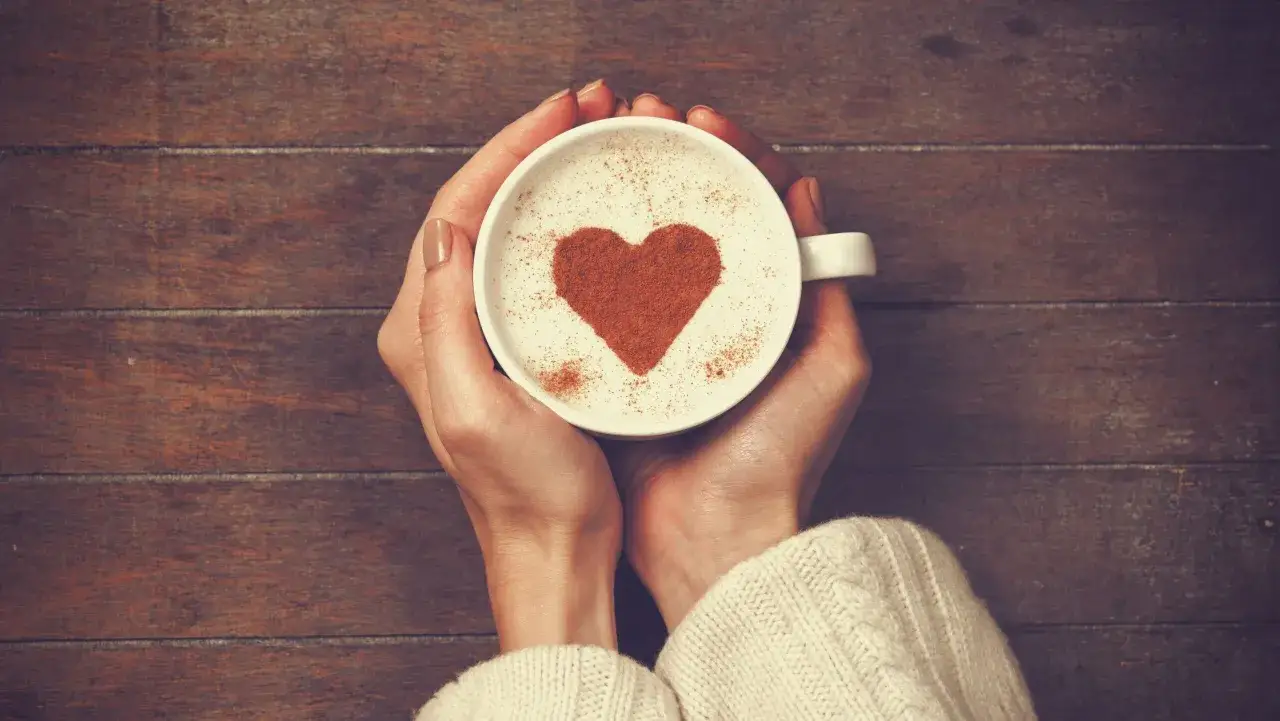 Mani che stringono una tazza di caffè con un cuore di cannella, perfetto per San Valentino.
