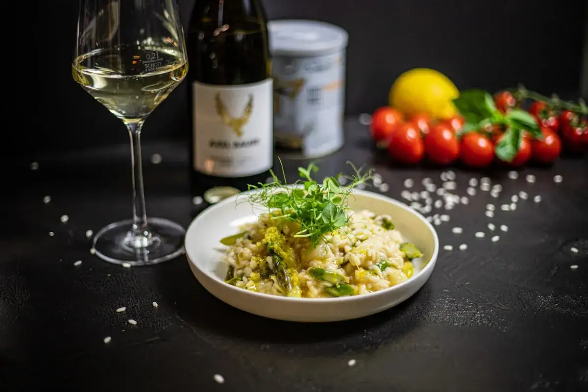 Kremowe risotto z kurczakiem i szparagami, udekorowane kiełkami. Obok kieliszek białego wina i butelka.