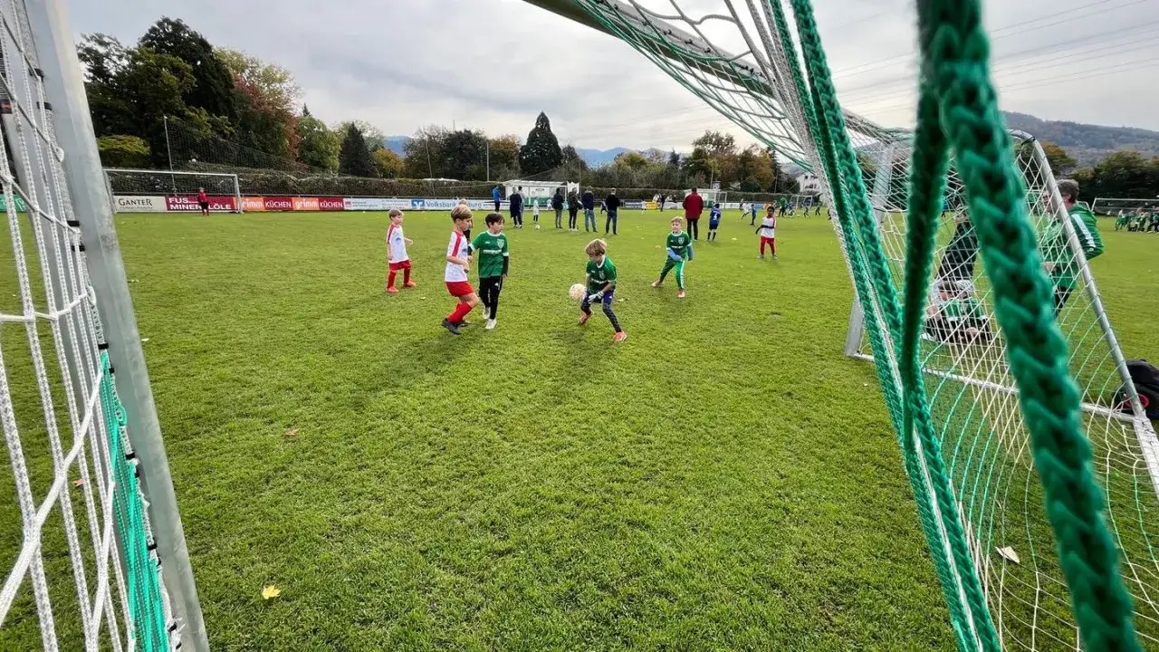 Kinder trainieren auf einem **funino feld**. Ein Junge im grünen Trikot dribbelt den Ball, während andere Kinder auf dem Rasen spielen.