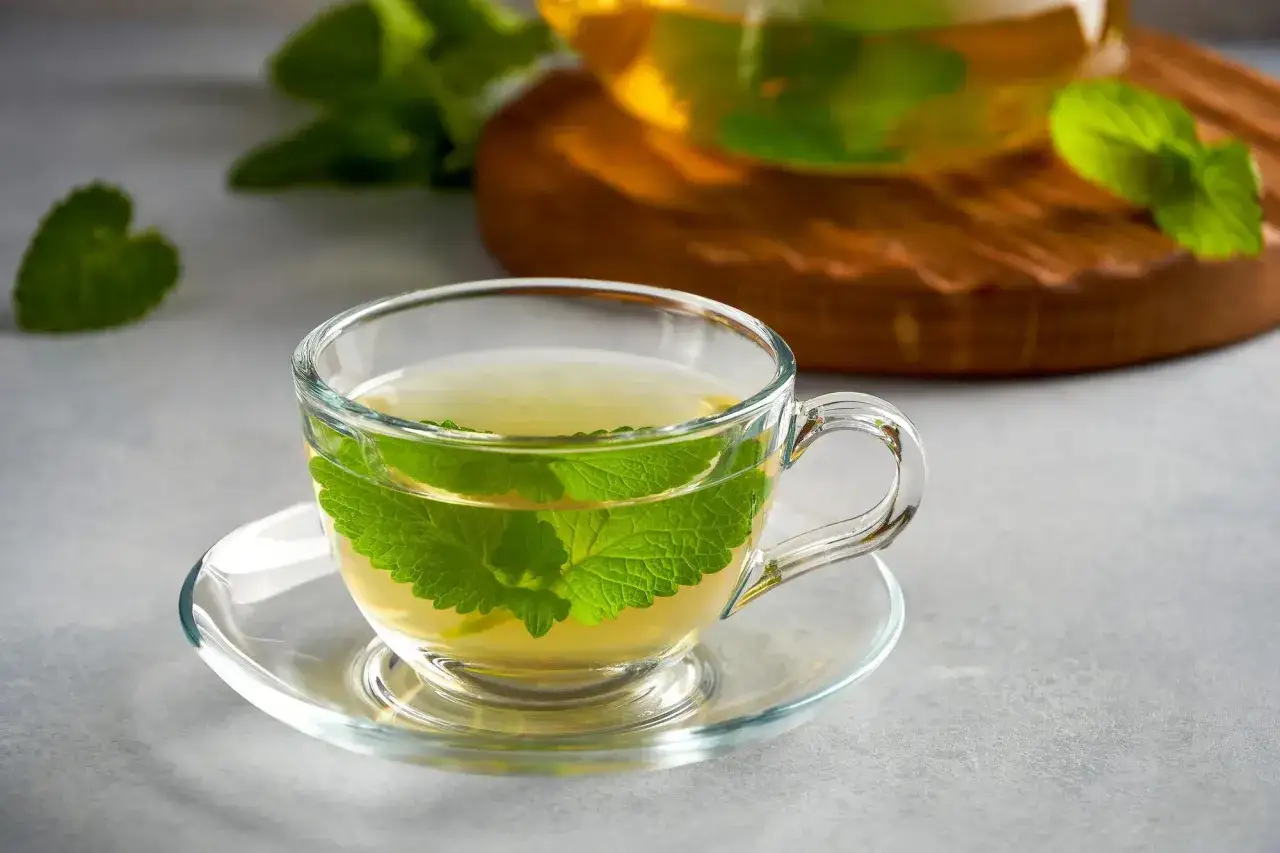 Aromatic melisa w szklanej filiżance, z liśćmi melisy pływającymi w naparze. Zastanawiasz się, jak długo działa melisa? Ten napój to chwila relaksu.