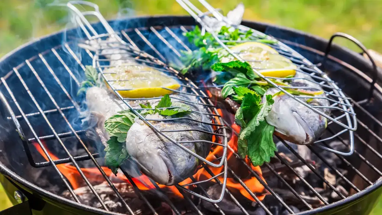 Zwei ganze Fische mit Zitrone und Kräutern auf einem Grillrost. So gelingt Fisch grillen ohne kleben.