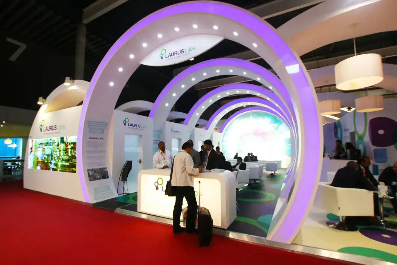 Expositores en un **roadshow que es** un evento de presentaci&oacute;n de Laurus Labs, con un dise&ntilde;o moderno y arcos iluminados en p&uacute;rpura.