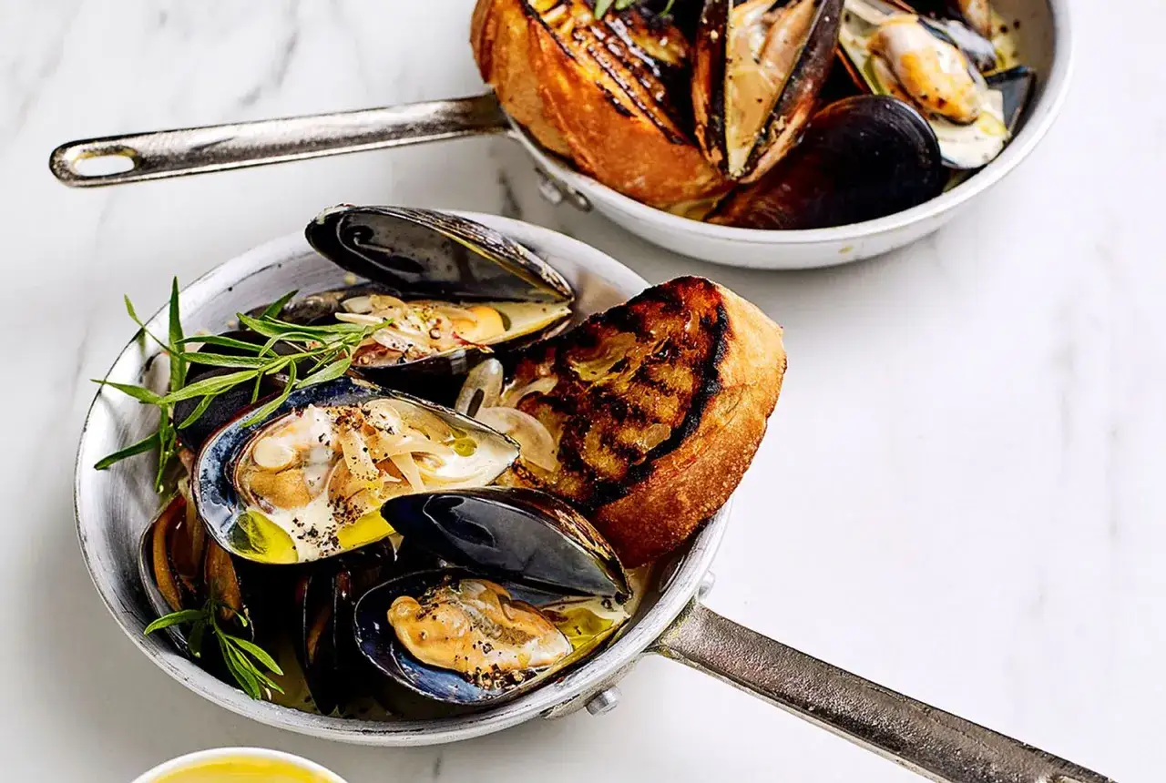 Zwei Pfannen mit dampfenden Muscheln und gegrilltem Brot. Perfekt f&uuml;r die Muschel Saison!