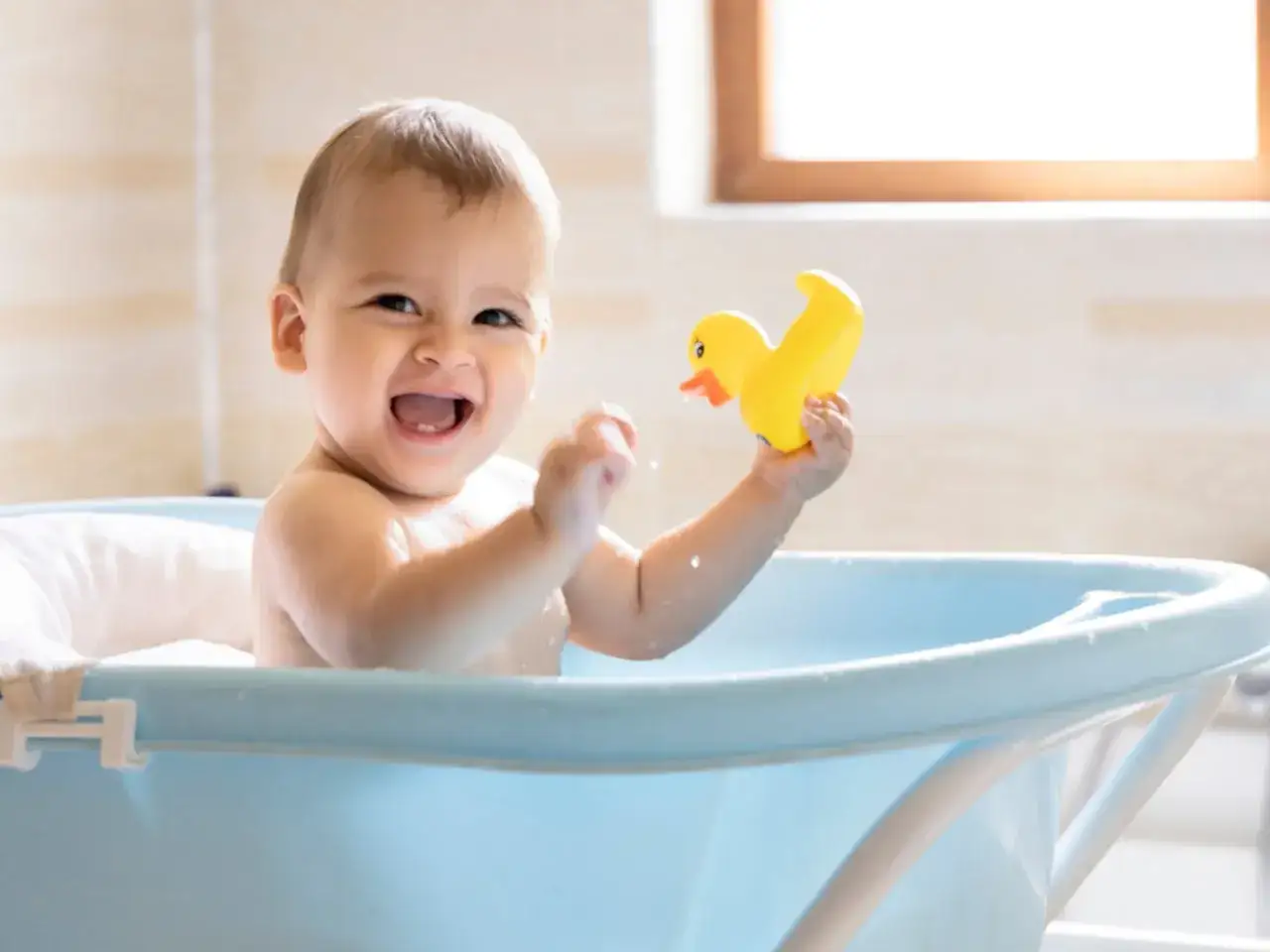 Un beb&eacute; sonriente juega con un patito de goma en la ba&ntilde;era. Es un buen momento para ba&ntilde;ar a un beb&eacute; despu&eacute;s de comer.