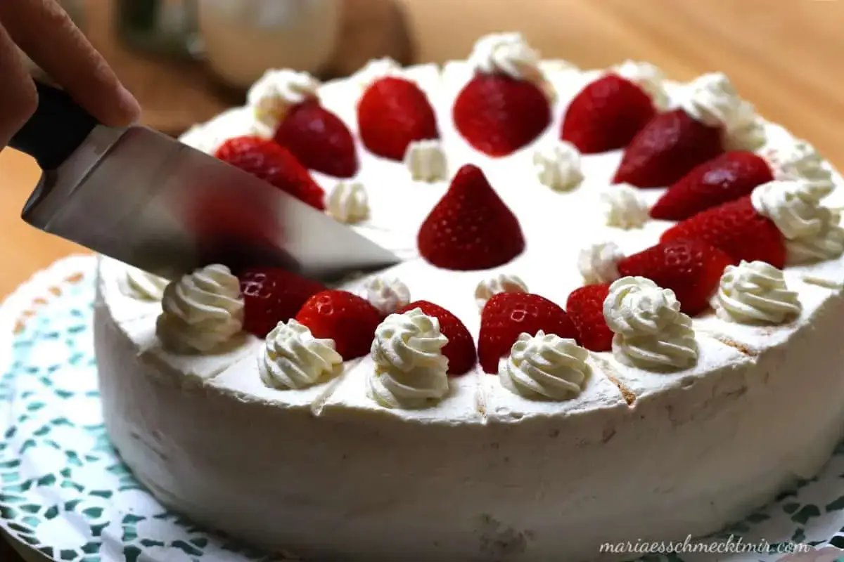Eine Messer schneidet in eine köstliche Erdbeer Sahne Torte, verziert mit frischen Erdbeeren und Sahnetuffs.
