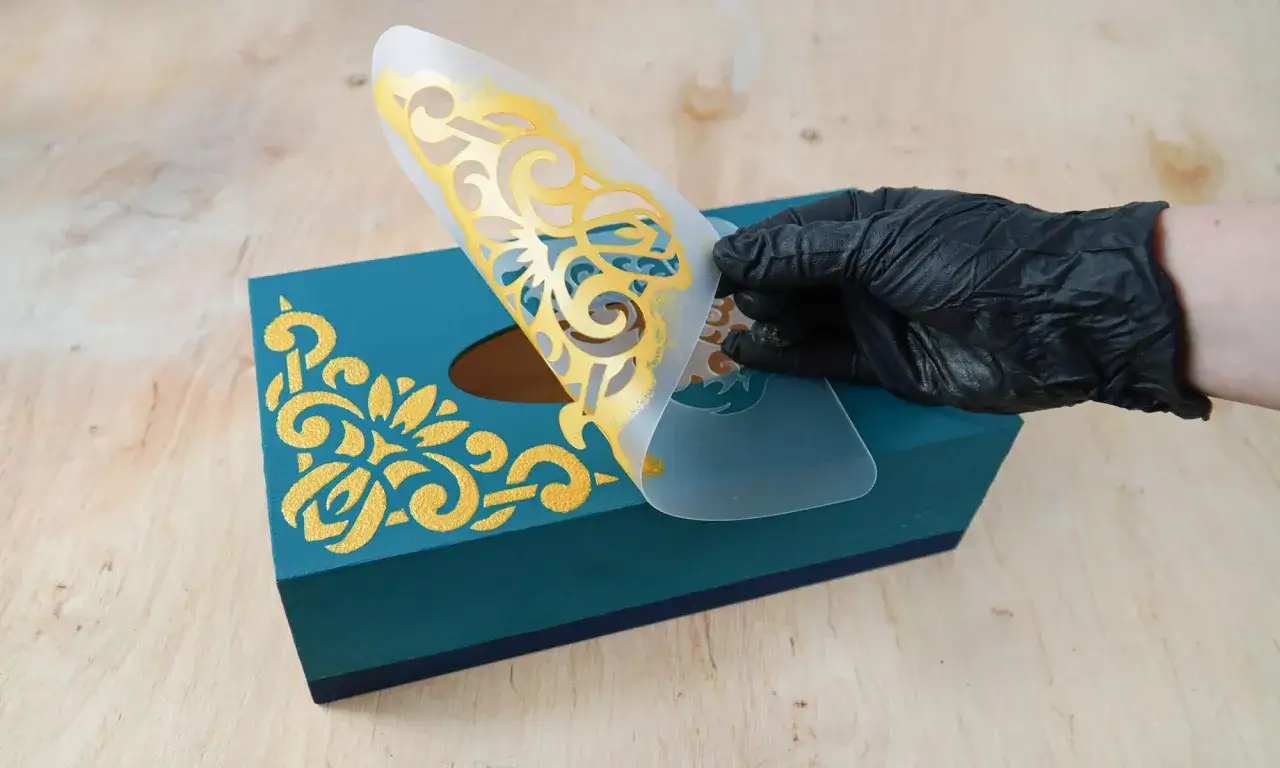 Maintenant, une id&eacute;e d&eacute;coration boite en bois : un pochoir dor&eacute; r&eacute;v&egrave;le un motif &eacute;l&eacute;gant sur une bo&icirc;te turquoise.